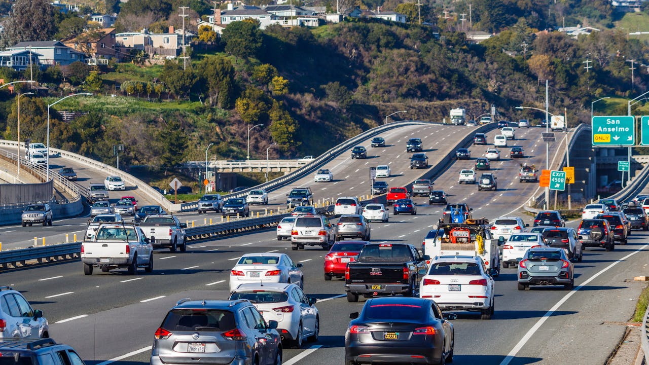 Busy multi-lane highway with heavy traffic flowing in both directions through hilly residential area with green road signs