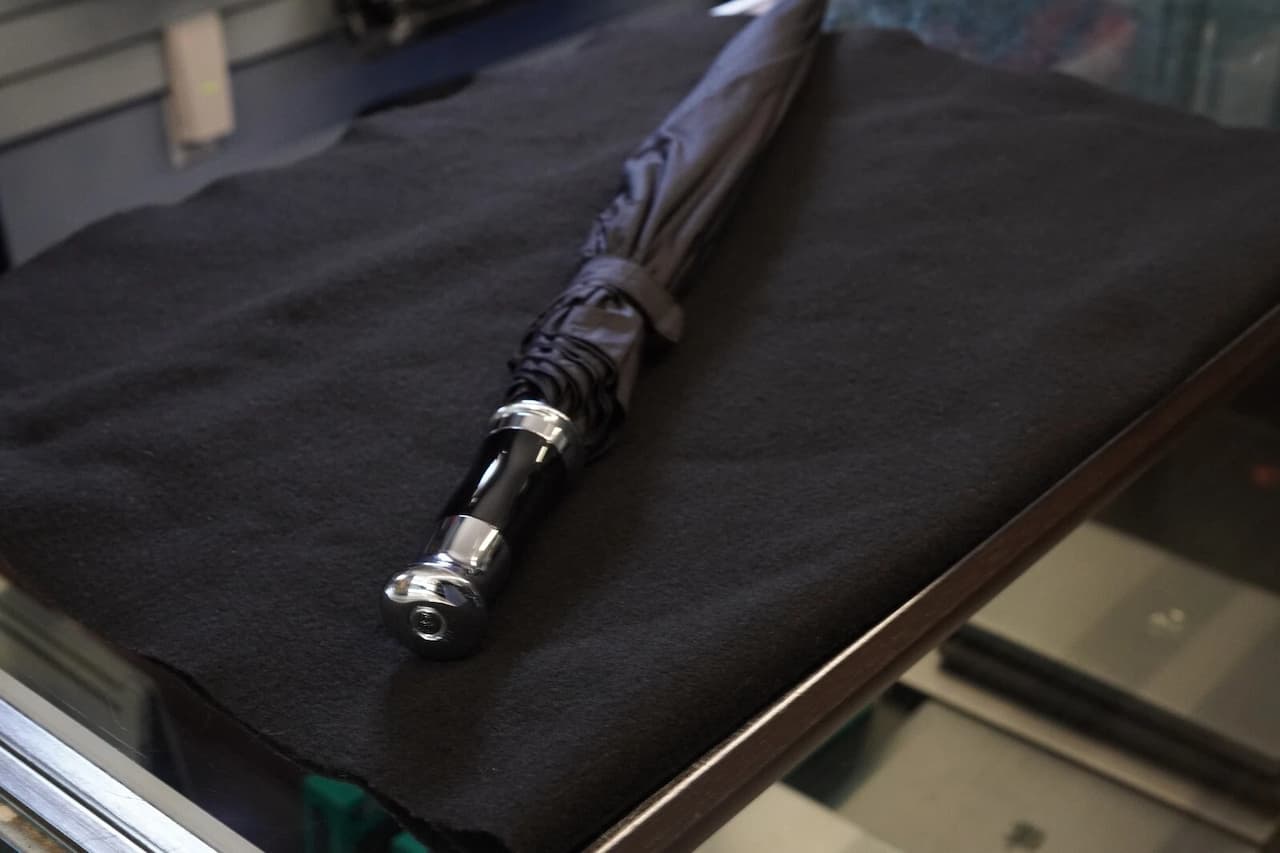 Black BMW Replacement Door umbrella with silver handle stored in dark foam compartment inside car trunk or storage area