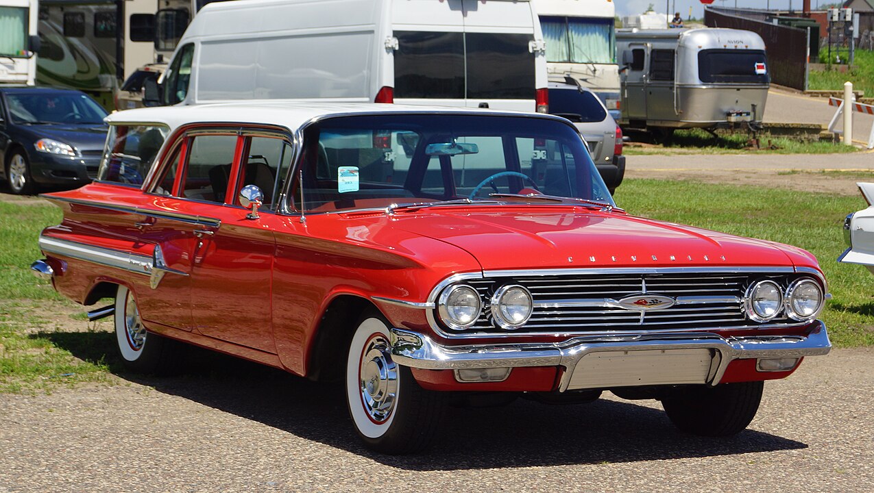 Red 1960 Chevrolet Nomad station wagon with chrome trim, whitewall tires, and dual headlights at outdoor car show