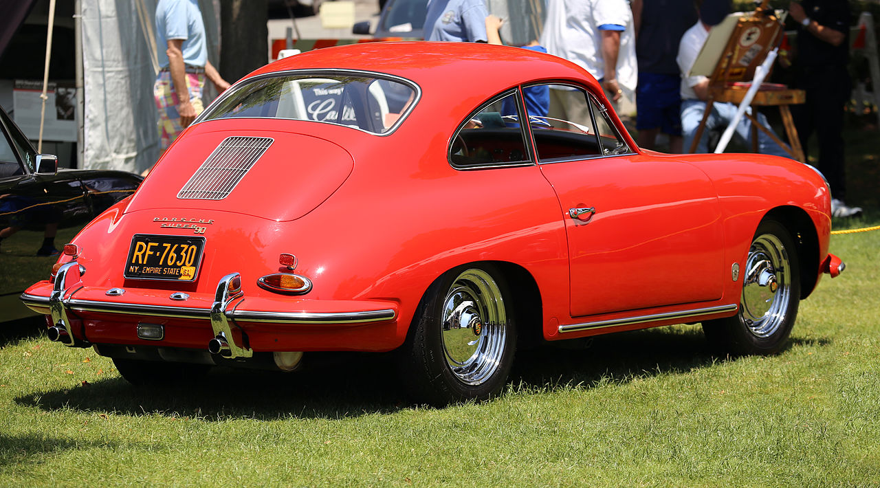 Classic red Porsche 356 with distinctive small rear window and chrome wheels at outdoor car show event