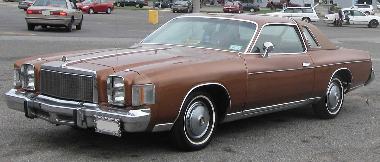 Brown 1978 Chrysler Cordoba classic car with white wall tires and chrome bumpers parked in busy parking lot