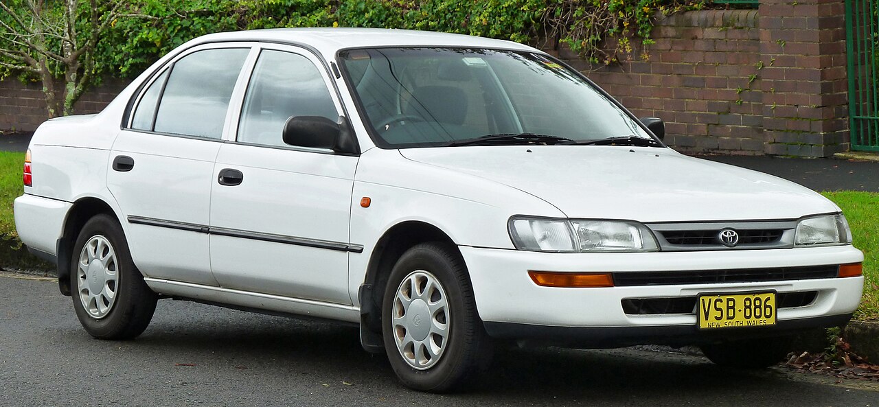 White 1994 Toyota Corolla sedan with New South Wales license plate parked on street near brick wall