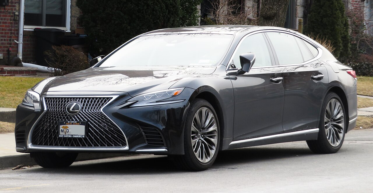 Dark gray Lexus LS 500 sedan with distinctive spindle grille parked on residential street near brick building
