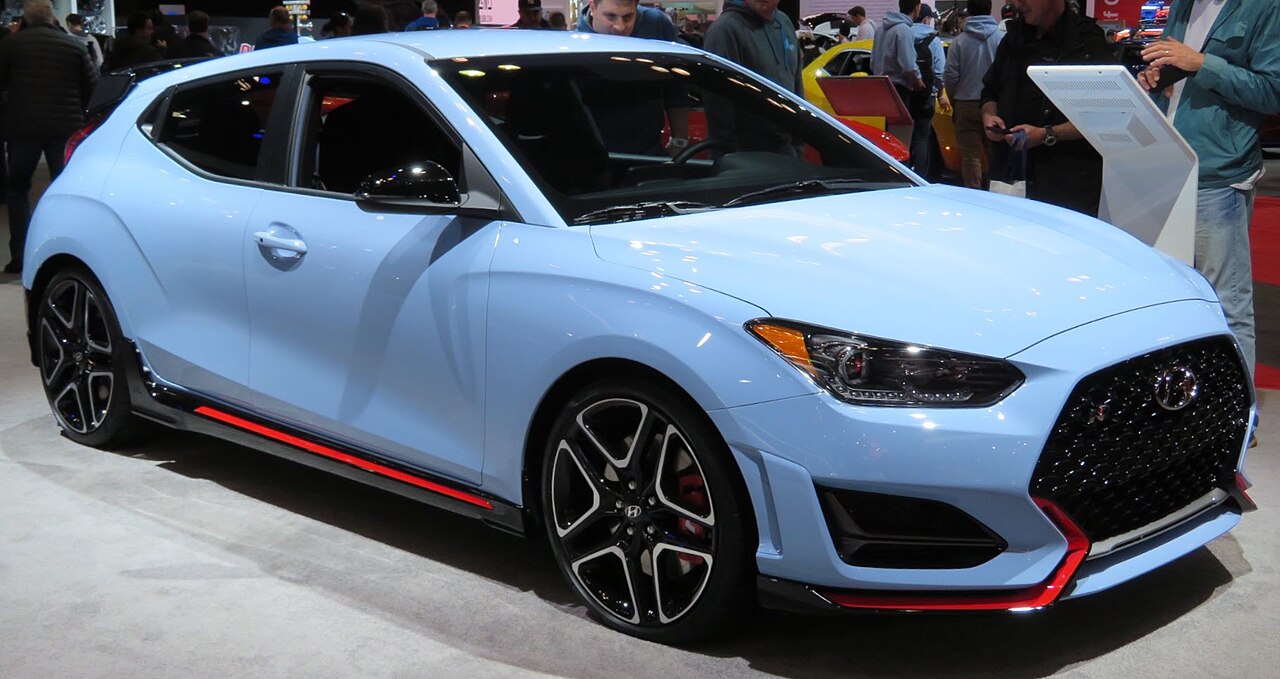 Light blue Hyundai Veloster N with red accents and sporty wheels displayed at indoor auto show
