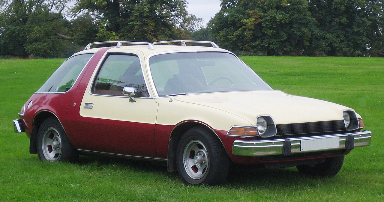 Cream and burgundy AMC Pacer classic car with distinctive wide body and large windows parked on green grass field