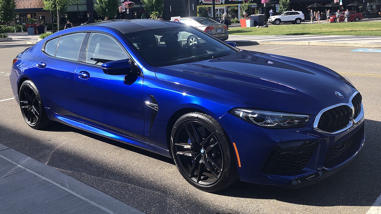 Bright blue 2020 BMW M8 Gran Coupe with black wheels parked on street in urban setting