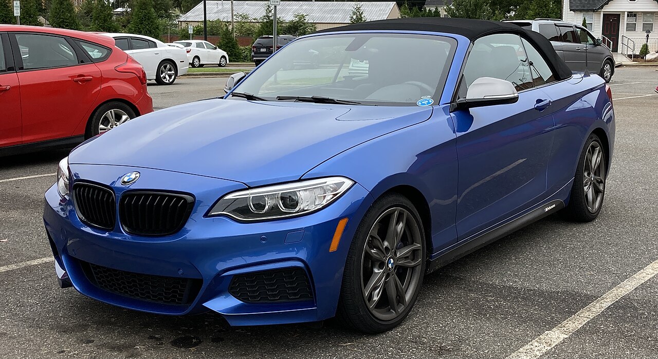 Blue BMW 2 Series convertible with black soft top parked in parking lot surrounded by other vehicles