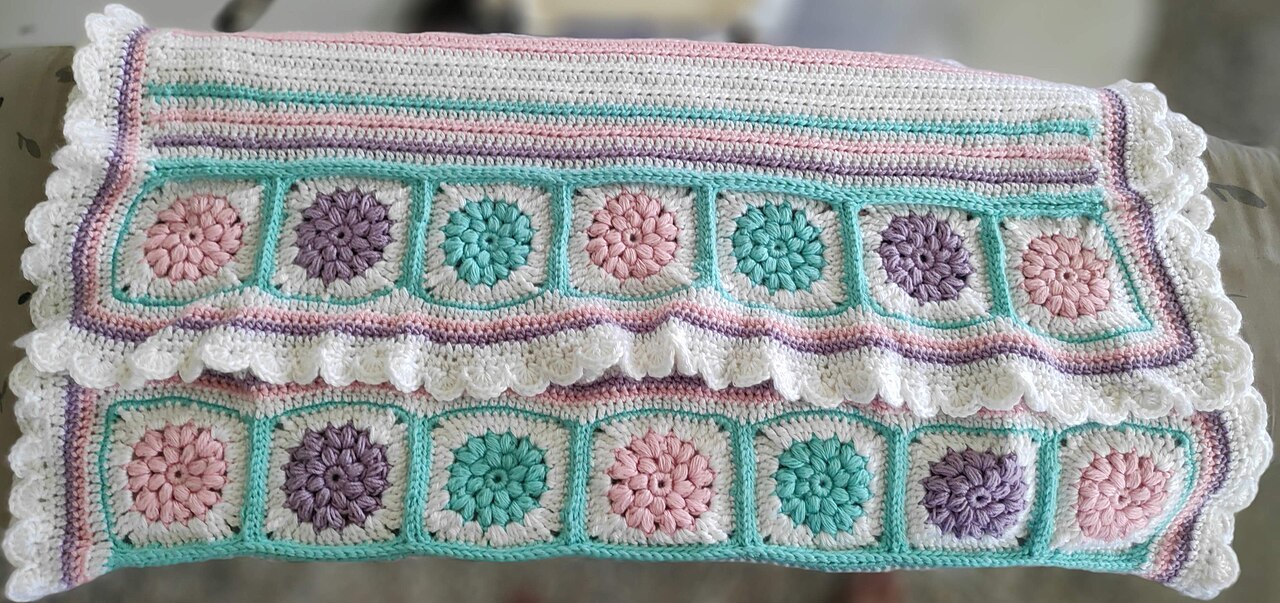 Handmade crocheted blanket with colorful granny squares in pink, purple, and teal with white scalloped border edges