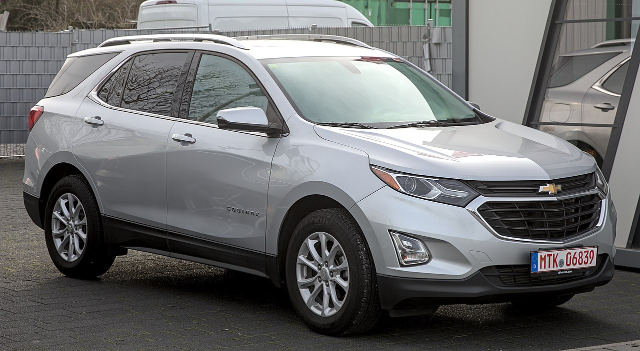 Silver Chevrolet Equinox SUV with chrome grille and alloy wheels parked on asphalt near modern buildings