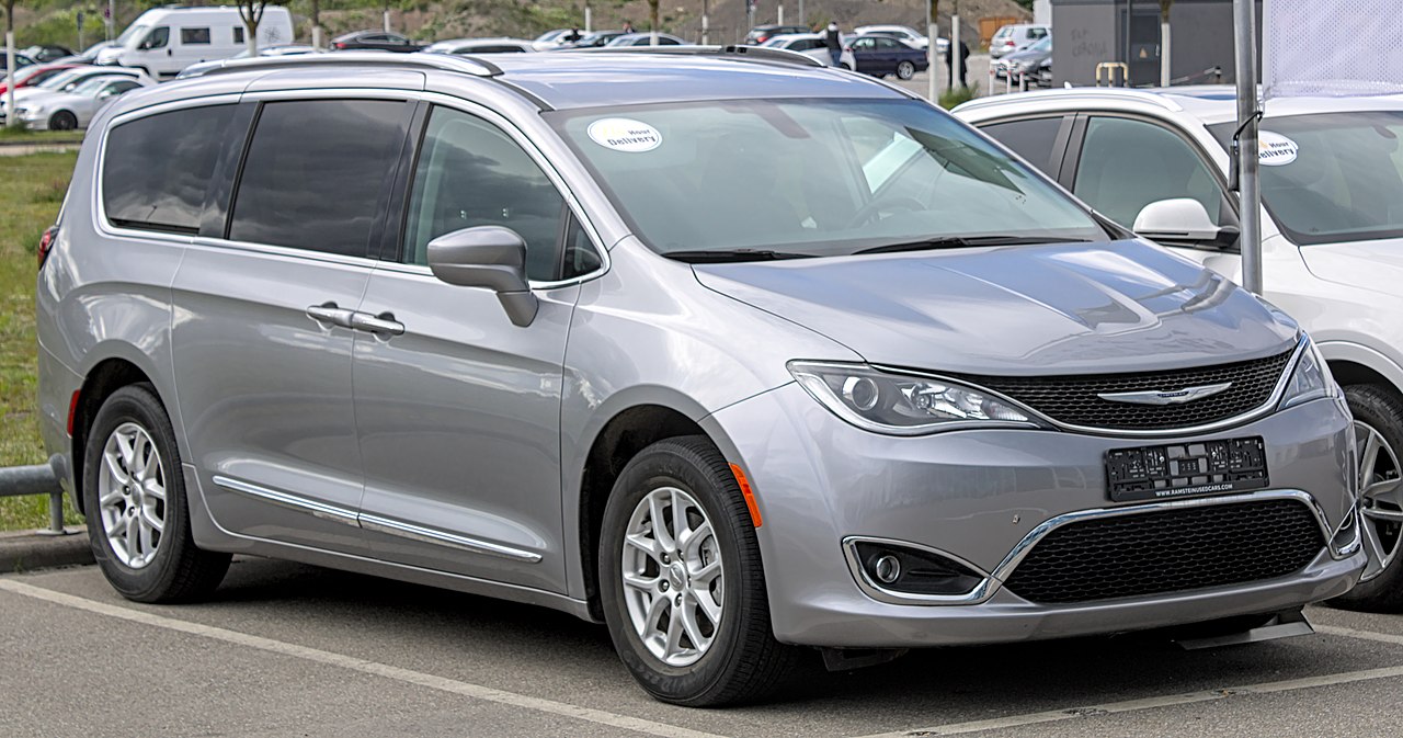 Silver 2021 Chrysler Pacifica minivan parked in dealership lot with other vehicles, featuring sliding doors and alloy wheels