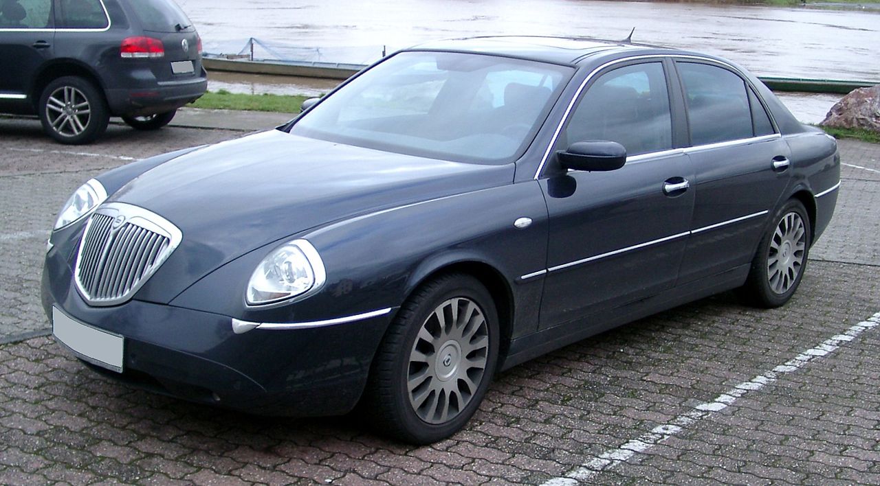 Dark blue Lancia Thesis luxury sedan with distinctive chrome grille and alloy wheels parked on cobblestone street