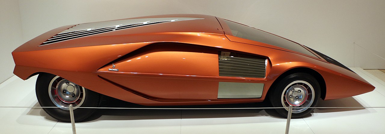 Orange wedge-shaped Lancia Bertone Stratos HF Zero concept car with triangular profile displayed in museum on white floor