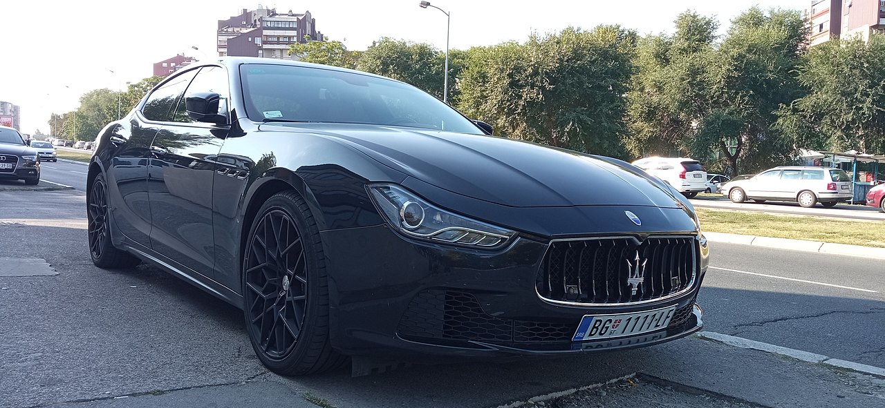 Black Maserati Ghibli sedan parked on city street with distinctive trident grille and black alloy wheels