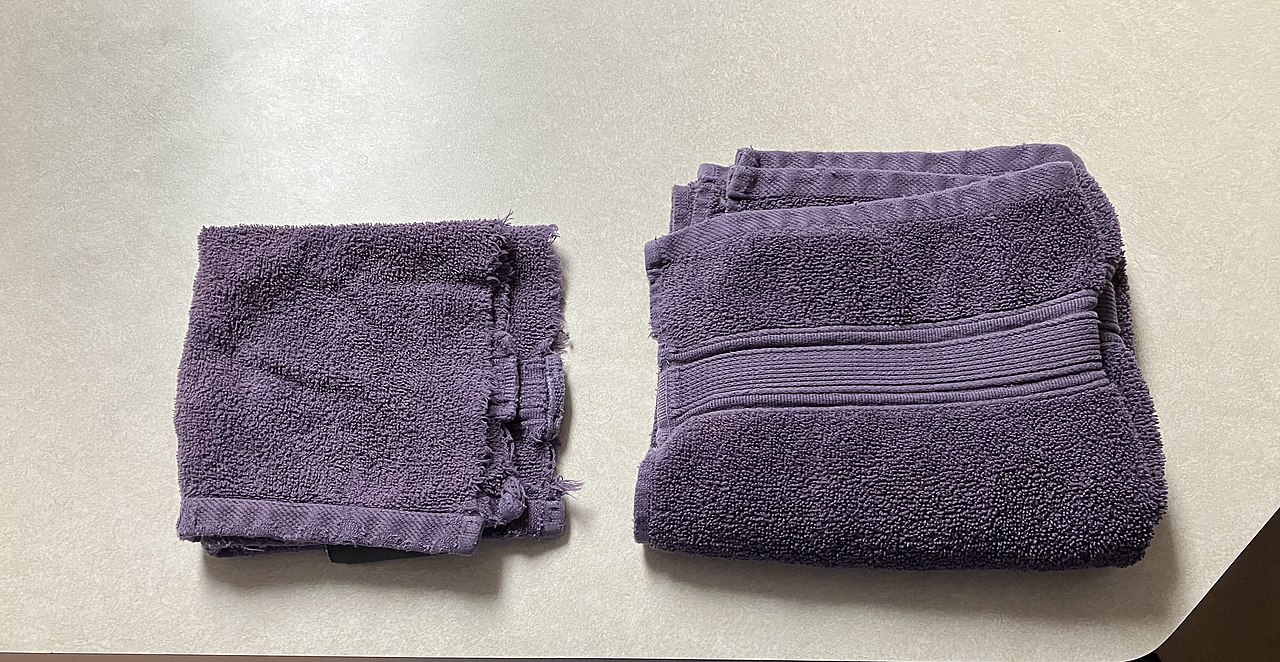 Two purple towels on beige surface - one folded neatly with ribbed trim, one torn and damaged with frayed edges