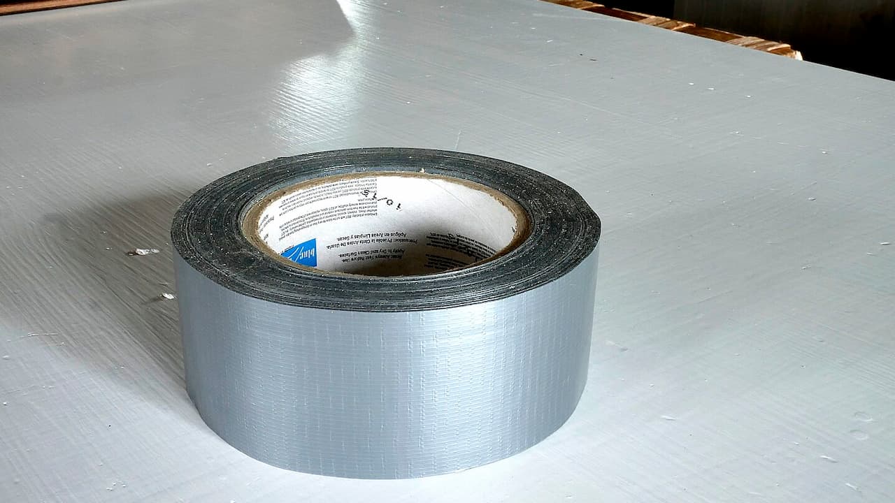 Silver duct tape roll with white label on white surface showing adhesive backing and brand markings