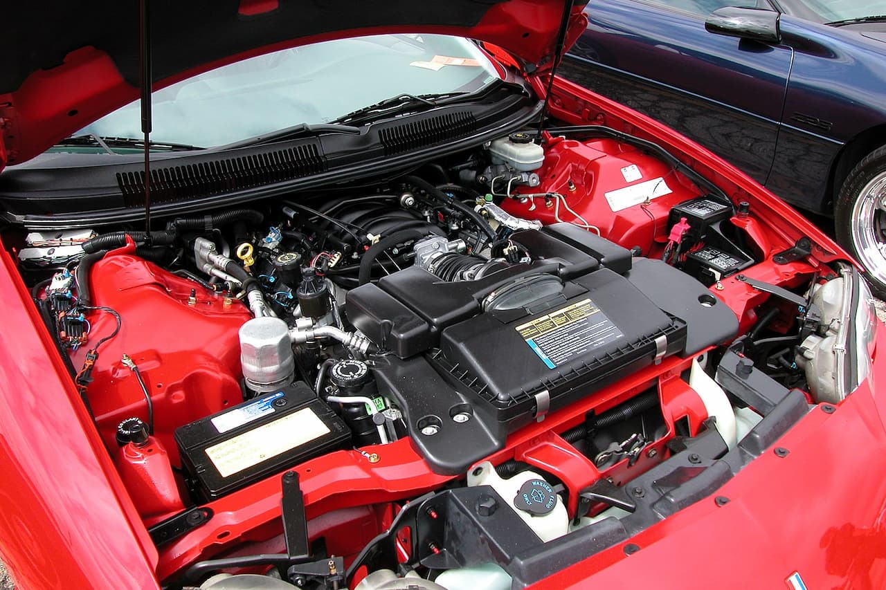 Red Chevrolet engine bay with open hood showing LS series V8 engine, air intake system, battery, and various automotive components