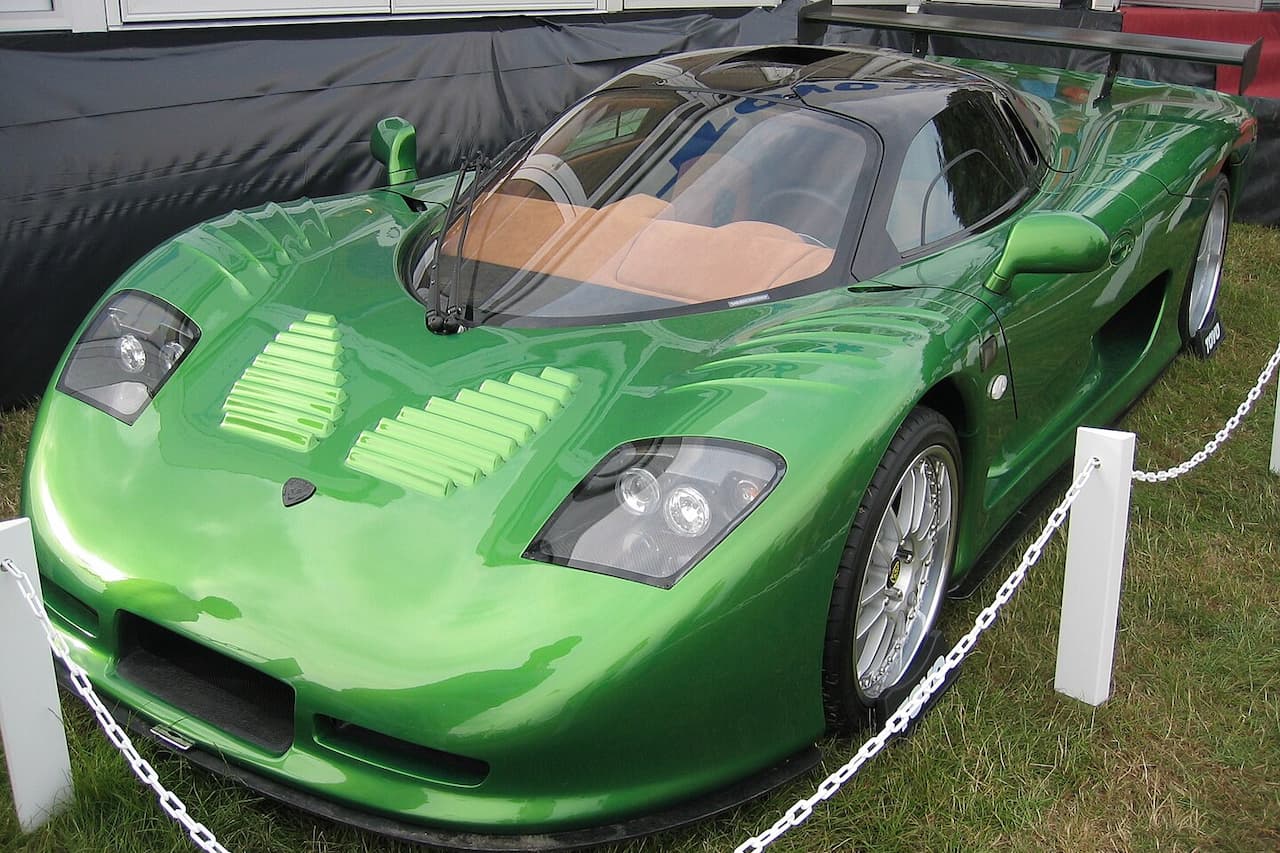 Bright green Mosler MT900 supercar with distinctive air vents and open cockpit displayed behind chain barriers
