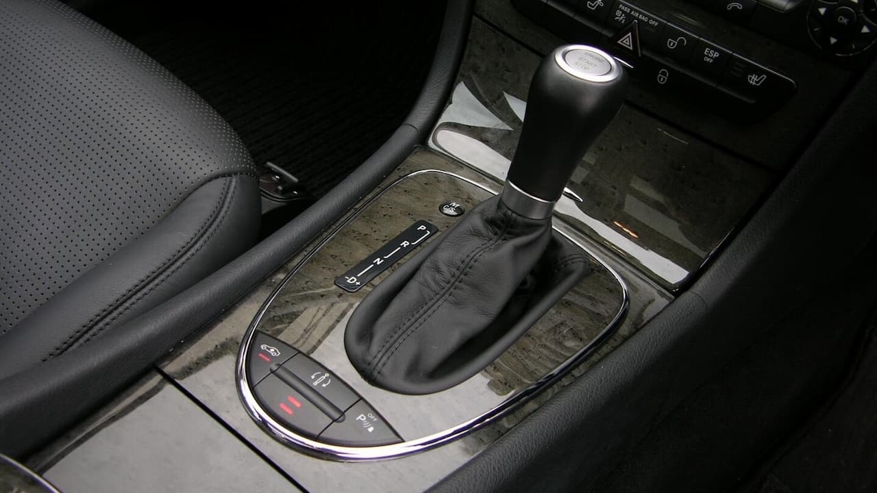 Car interior showing automatic transmission gear selector with leather boot, wood grain trim, and electronic controls in center console