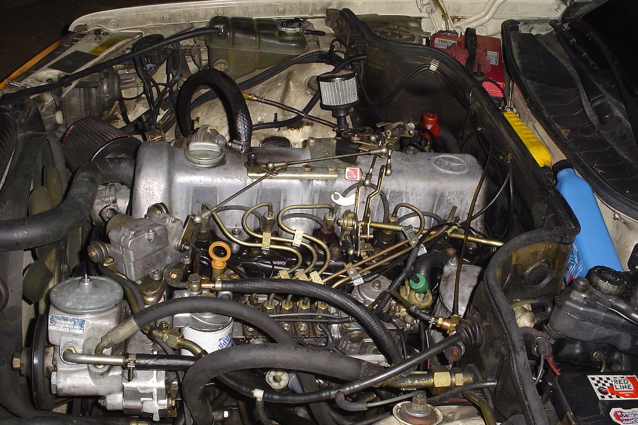 Mercedes-Benz OM617 diesel engine bay showing silver engine block, fuel injection system, vacuum lines, and various mechanical components
