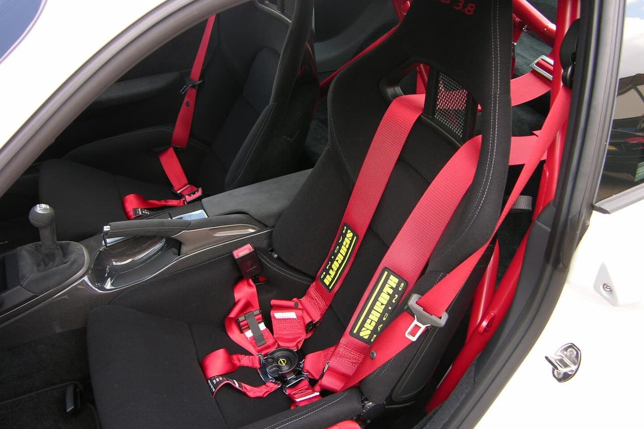 Racing racing bucket seat with red and black upholstery, five-point safety harness system, and roll cage in sports car interior