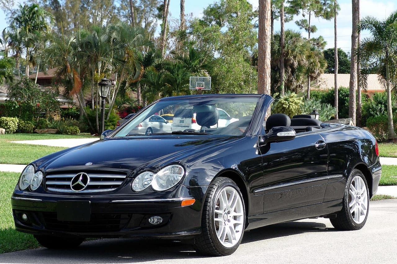 Black Mercedes-Benz CLK convertible with silver alloy wheels parked on residential street with palm trees and tropical landscaping