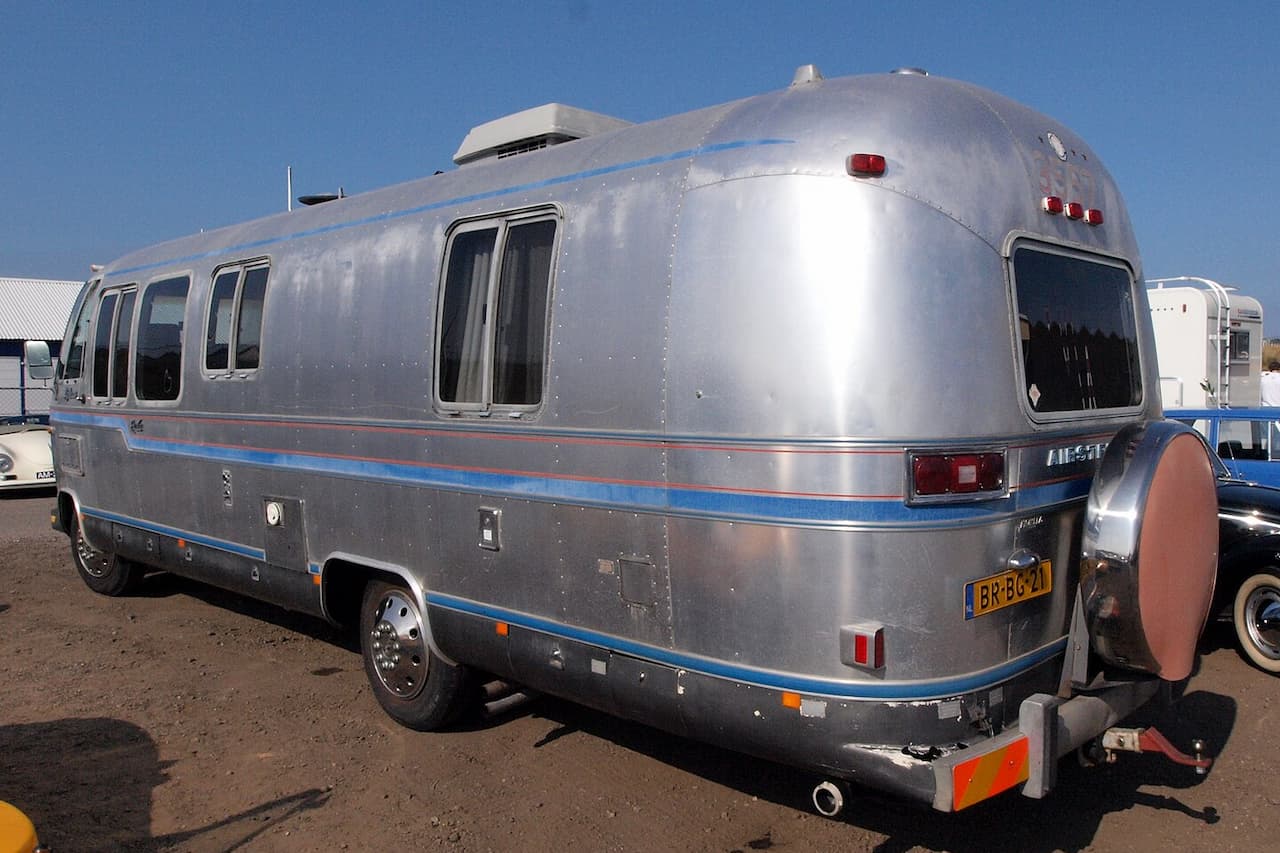 Silver Airstream Classic travel trailer with blue trim and multiple windows parked in RV lot under blue sky