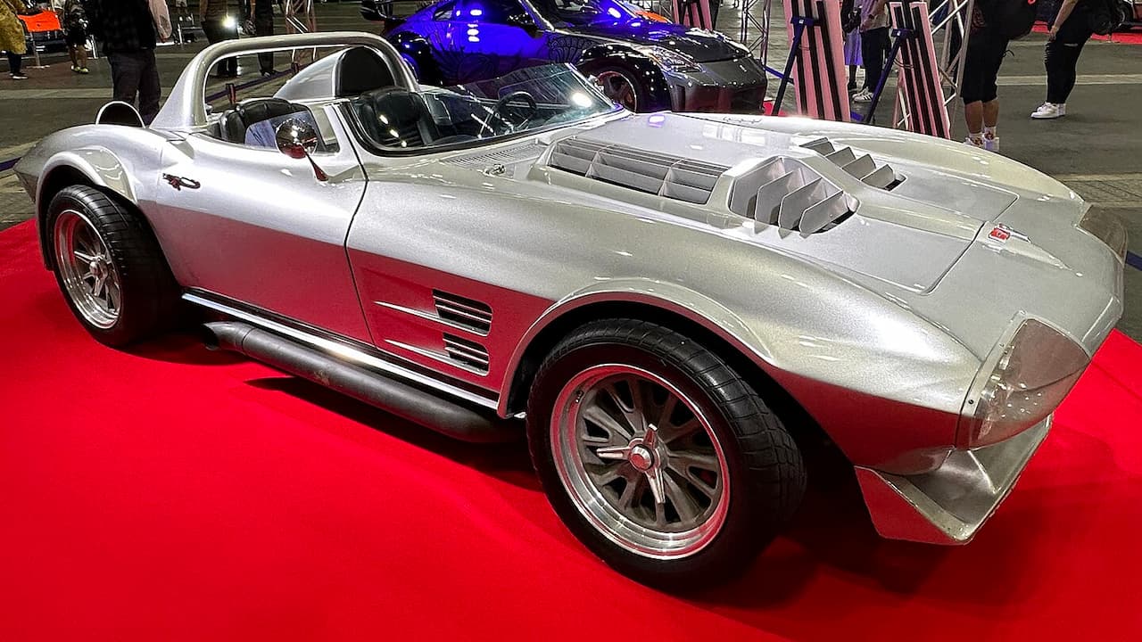 Silver Chevrolet Corvette C2 Grand Sport with red accents and side exhaust pipes displayed on red carpet at auto show