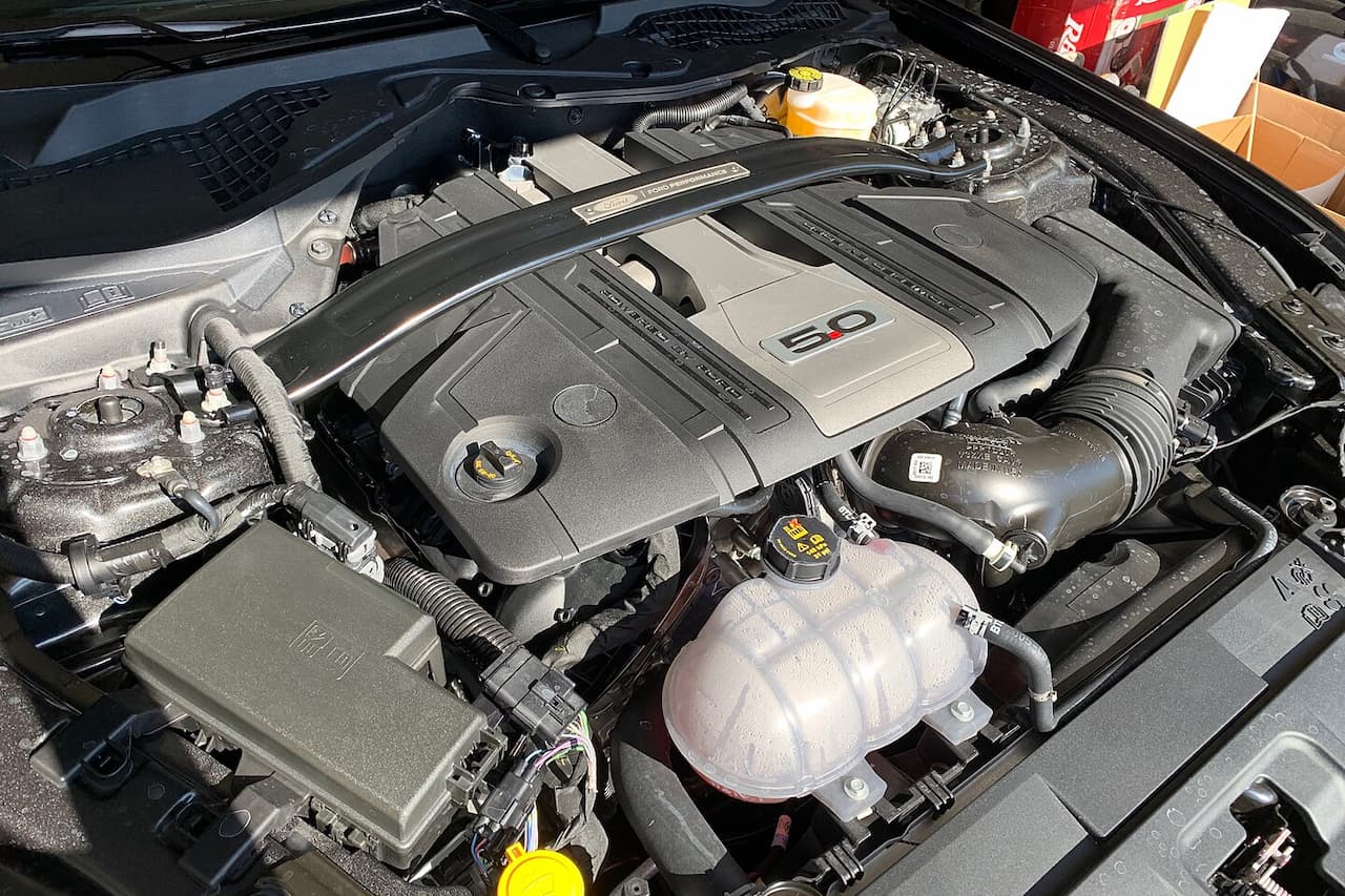 Ford Coyote V8 engine bay showing 5.0-liter motor with plastic engine covers, air intake, fluids reservoir, and various engine components