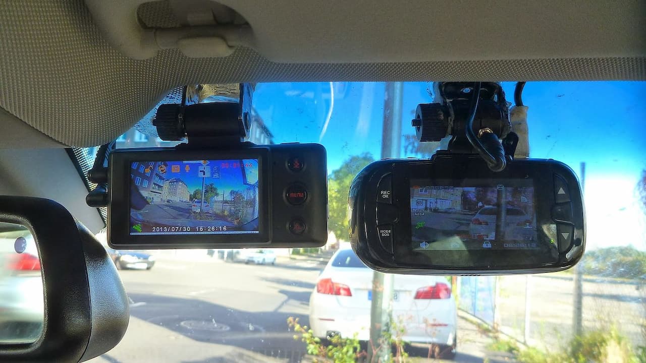 Two dash cameras mounted on car rearview mirror displaying recorded footage of road with timestamp and traffic