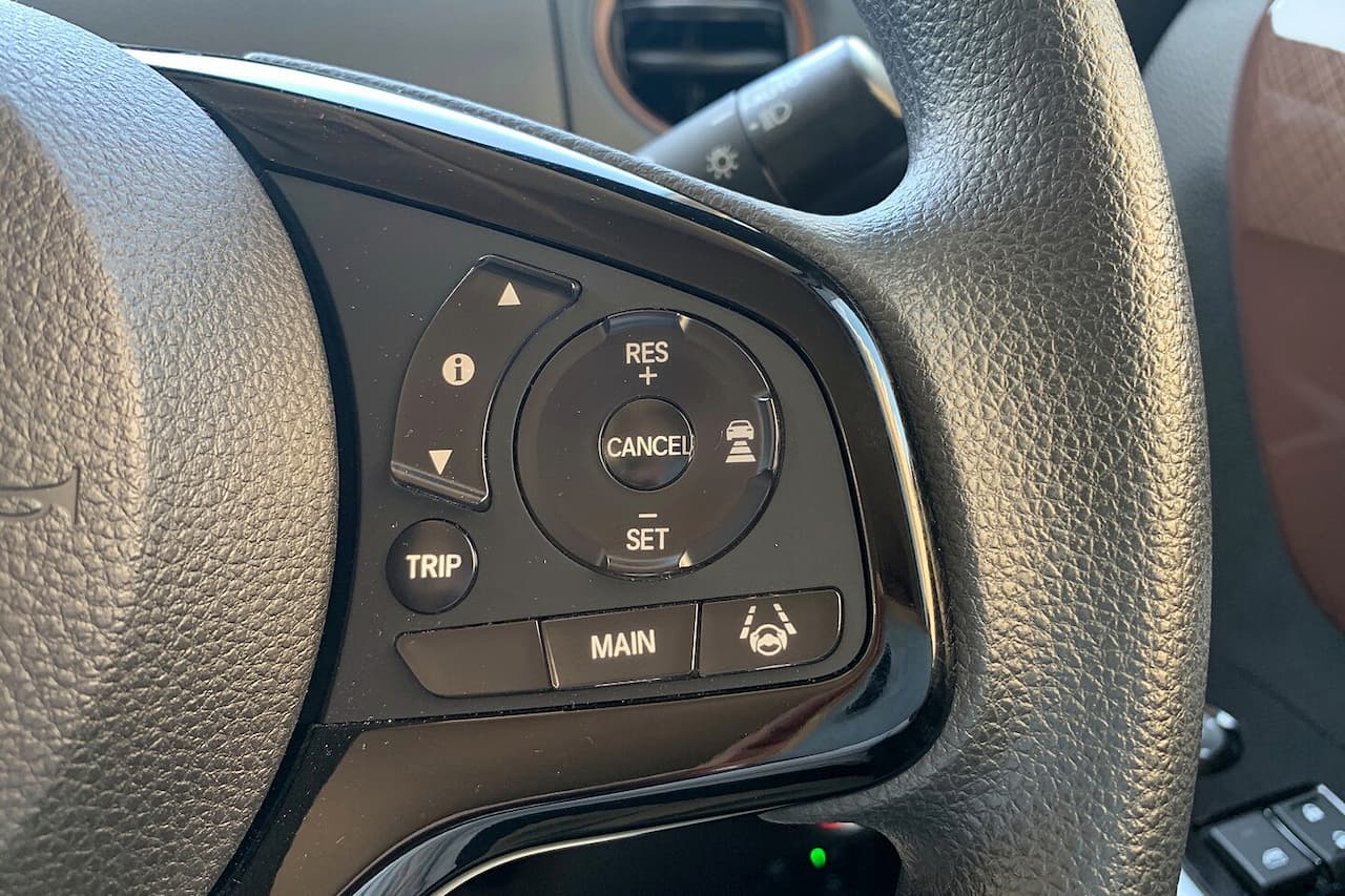Steering wheel-mounted adaptive cruise control buttons including RES/SET, CANCEL, TRIP, MAIN, and distance adjustment controls on leather wheel