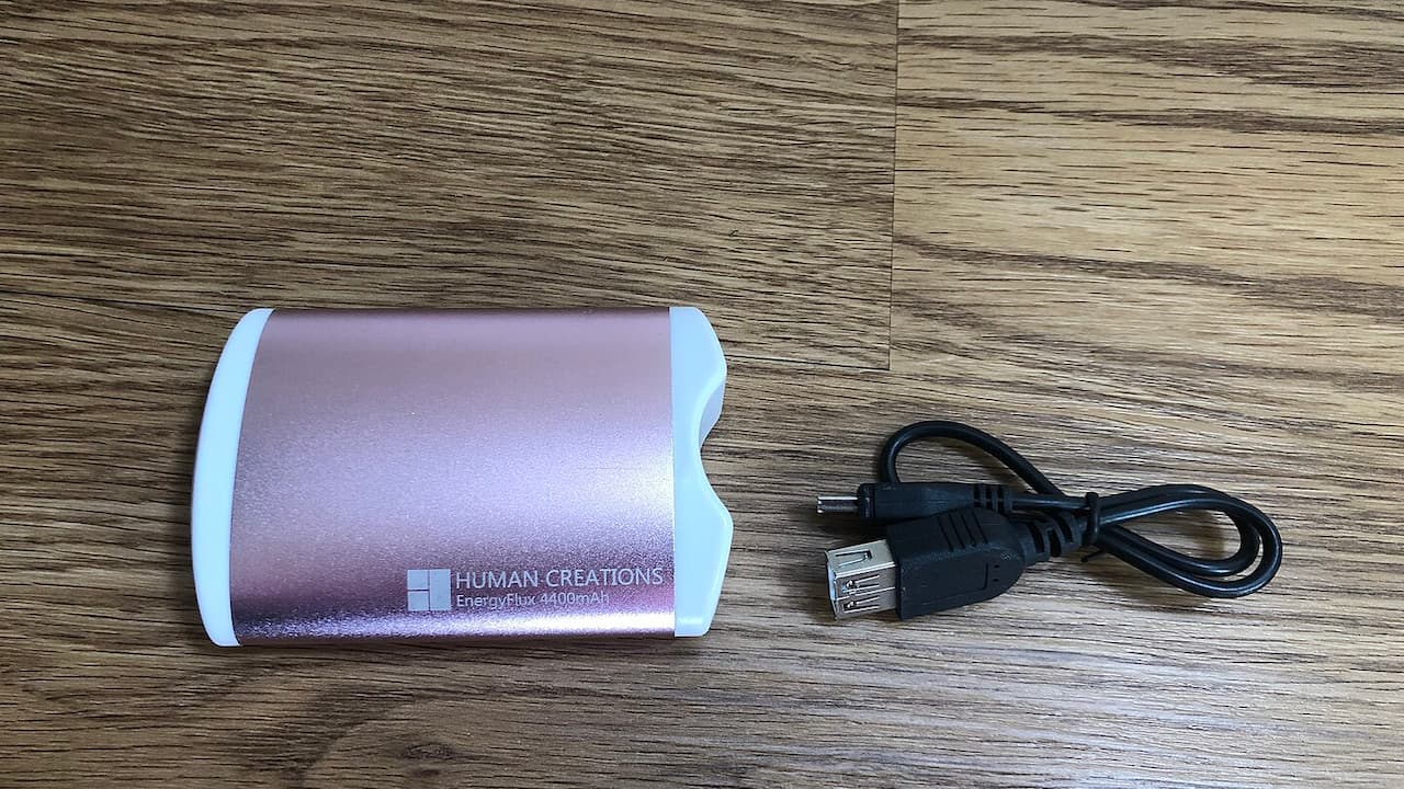 Purple gradient portable charger with white ends labeled "Human Creations EnergyFlux 4400mAh" beside black USB cable on wood surface