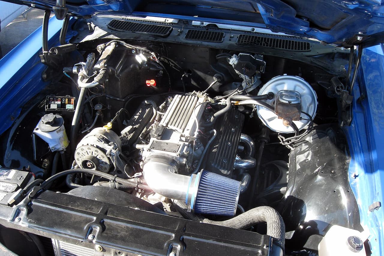 Chevrolet small block V8 engine bay in blue car showing finned valve covers, alternator, cold air intake, and various engine components