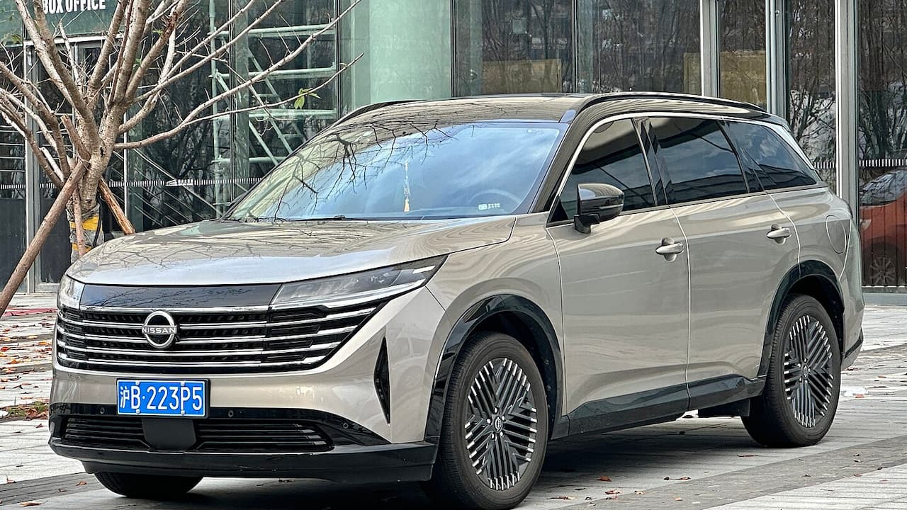 Silver Nissan Pathfinder SUV with distinctive grille and turbine-style wheels parked outside modern glass building with Chinese license plate