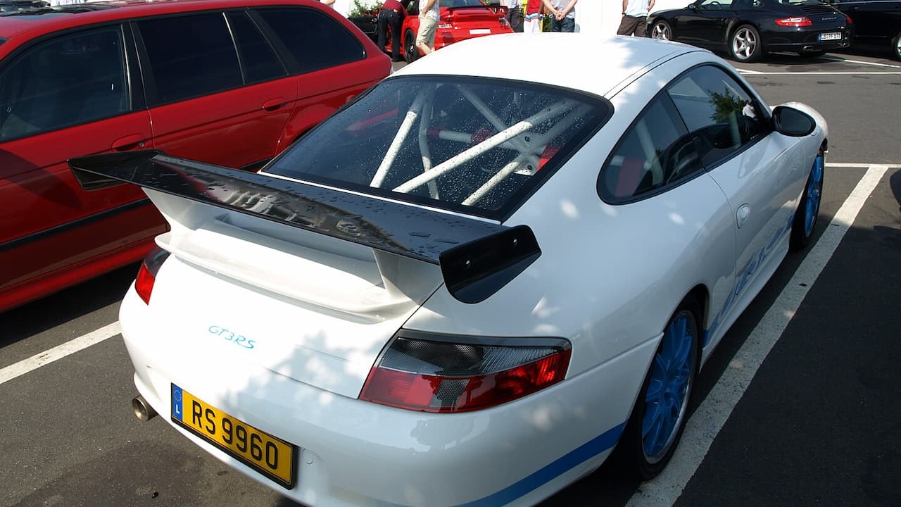 White Porsche GT3 RS with visible roll cage through rear window, large spoiler, parked at car meet event