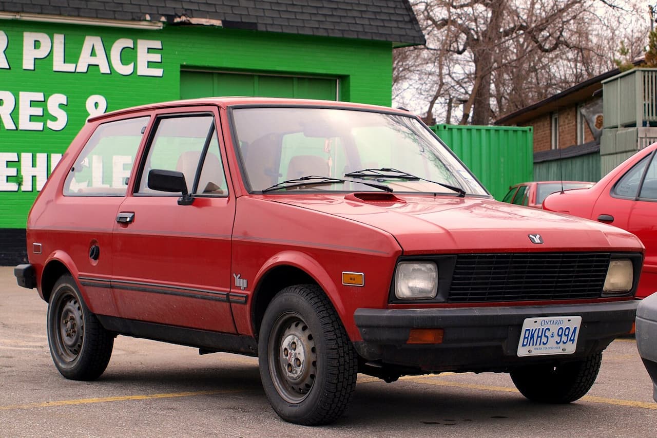 Red Yugo GV compact car with Ontario license plate "BKHS-994" parked on street with green building in background