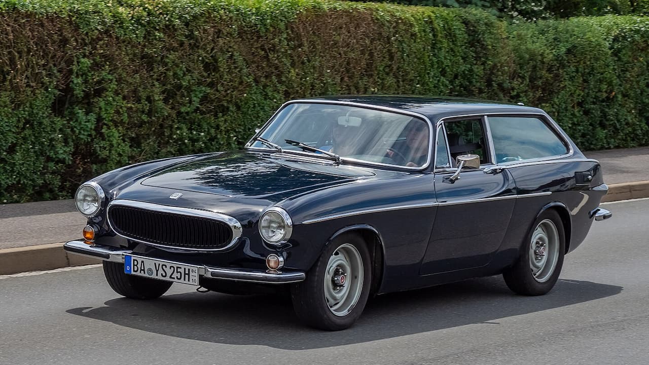Black Volvo P1800 ES shooting brake with German license plate parked on concrete with green foliage background