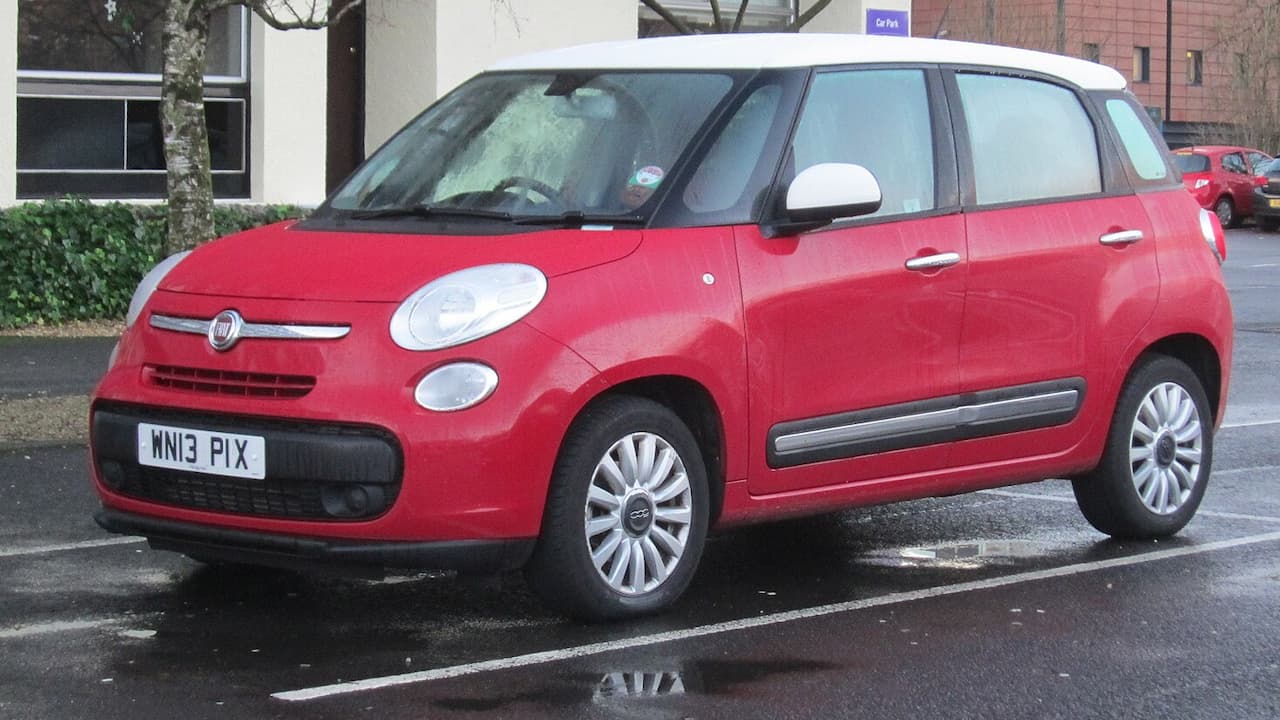 Red Fiat 500L compact MPV with white roof parked in wet parking lot with buildings in background