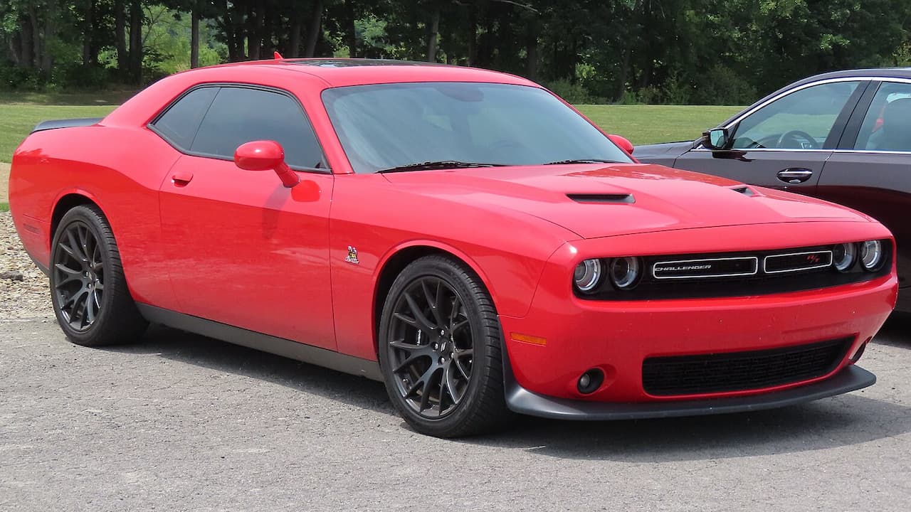 Red Dodge Challenger R/T Scat Pack with black wheels and hood scoop parked on asphalt
