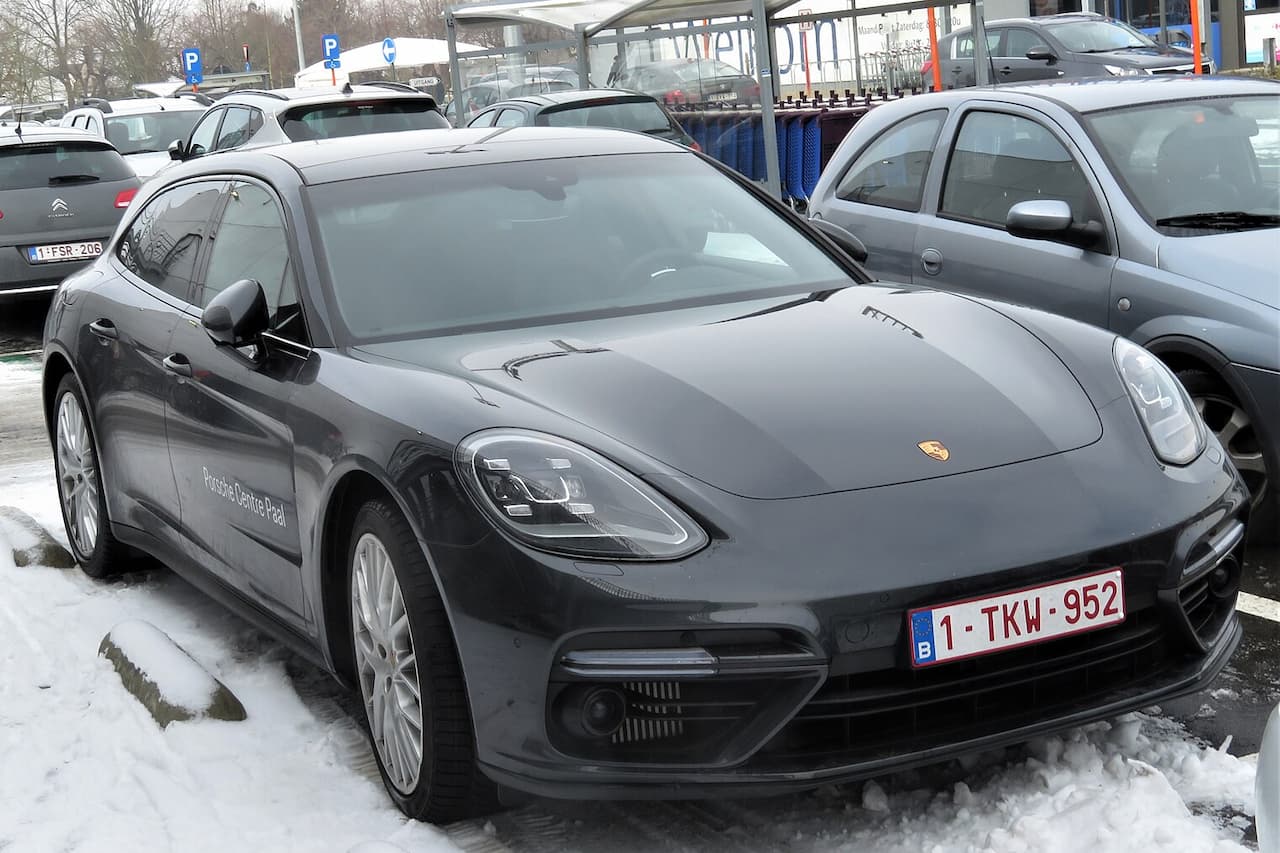 Black Porsche Panamera Sport Turismo parked in snowy parking lot with Belgian license plate, surrounded by other vehicles