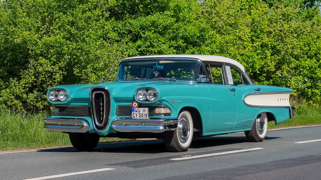 Turquoise and white vintage Edsel sedan with distinctive vertical grille parked on road beside green foliage