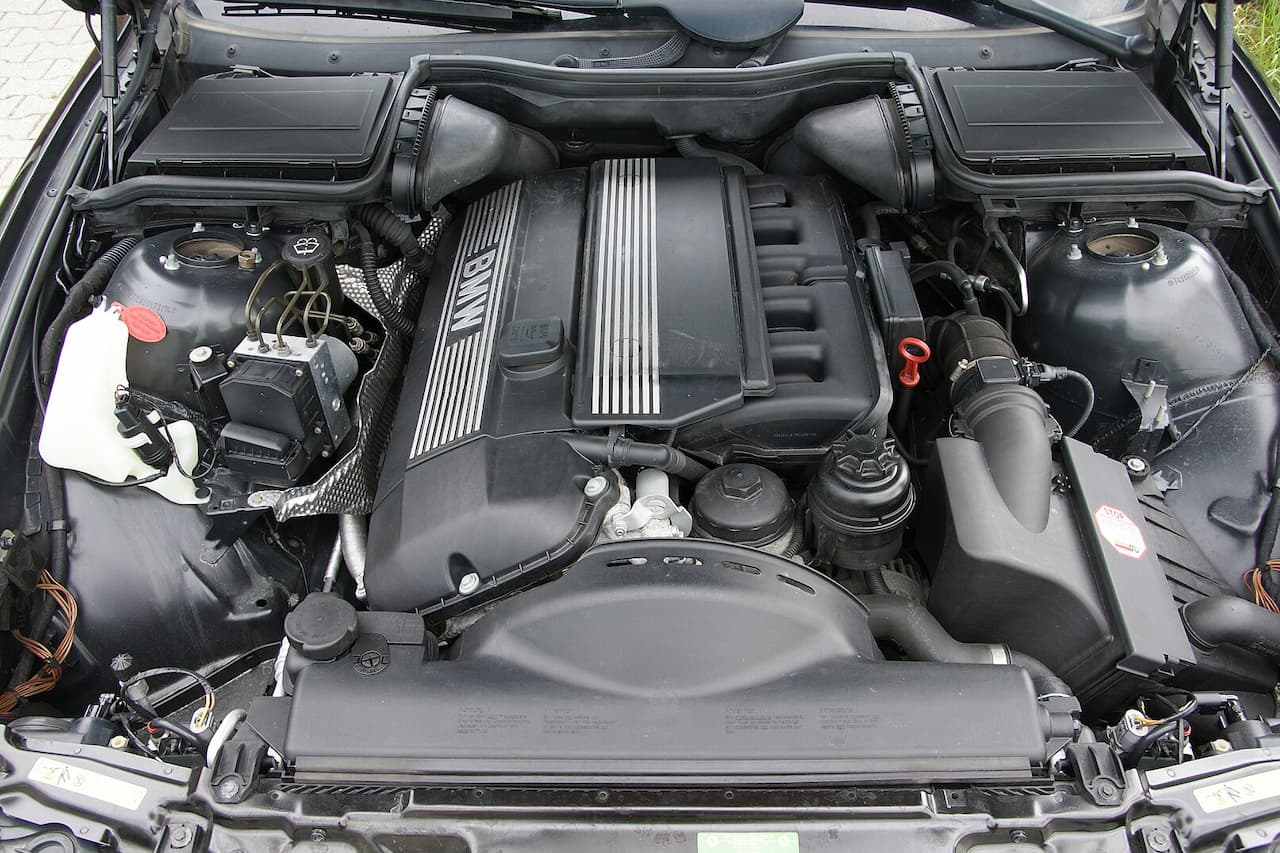BMW M54 inline-6 engine bay showing silver ribbed engine cover, air intake system, coolant reservoir, and various black engine components