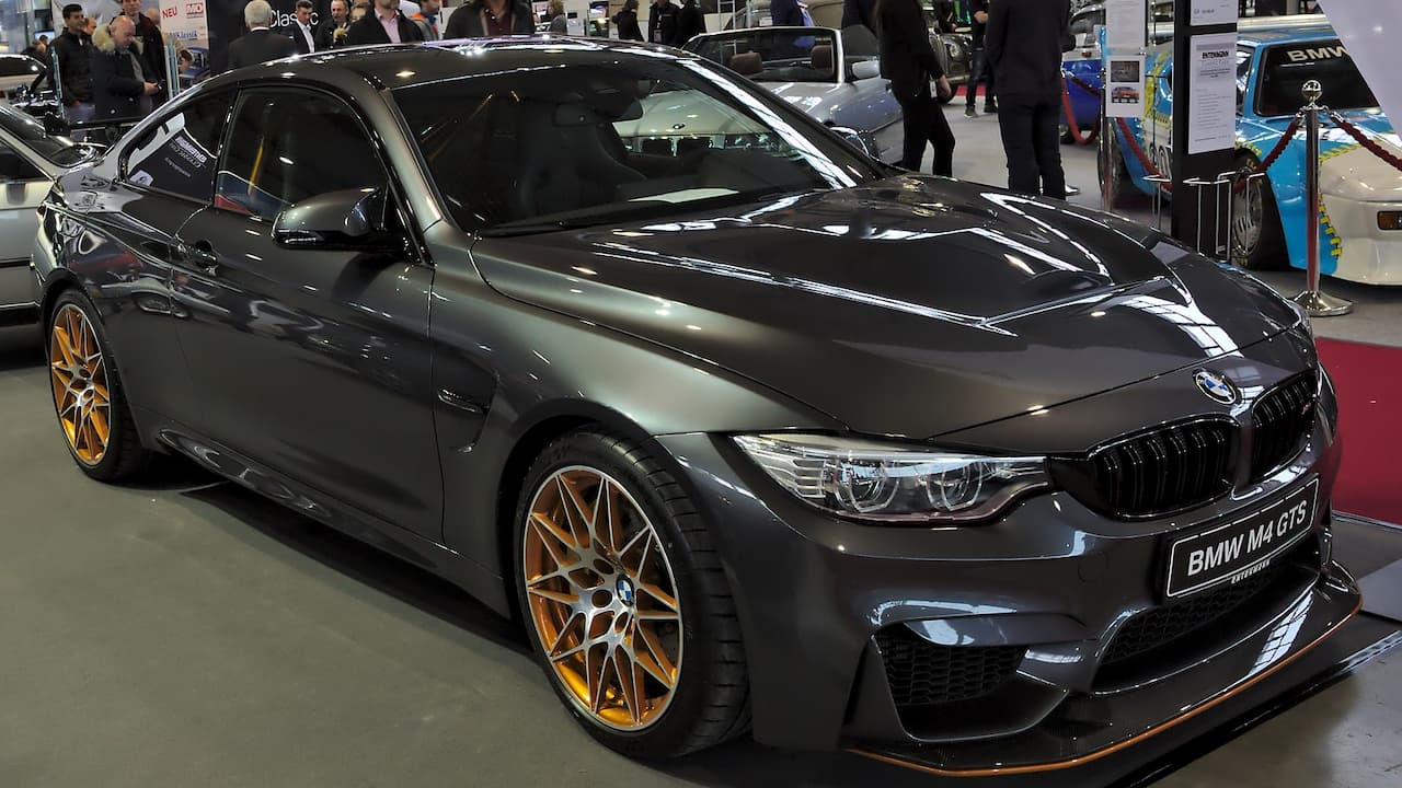 Gray 2018 BMW M4 GTS with gold wheels and aerodynamic body kit displayed at indoor auto show
