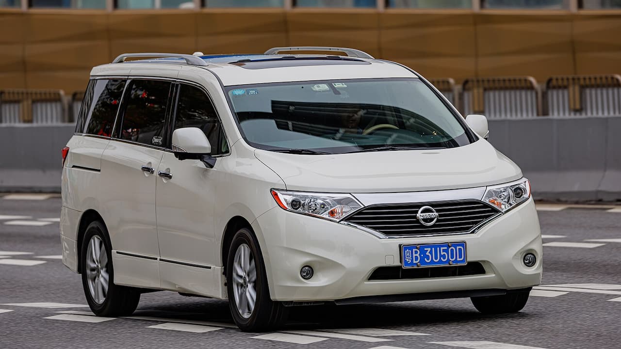 White 2022 Nissan Quest minivan with roof rails and Chinese license plate driving on paved road
