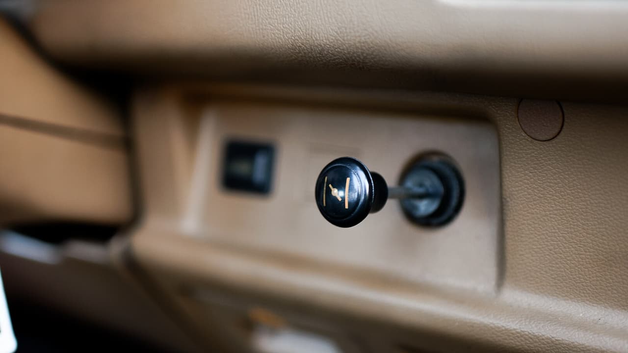 Car dashboard showing manual choke knob with golden emblem pulled out, alongside other control knobs in beige interior