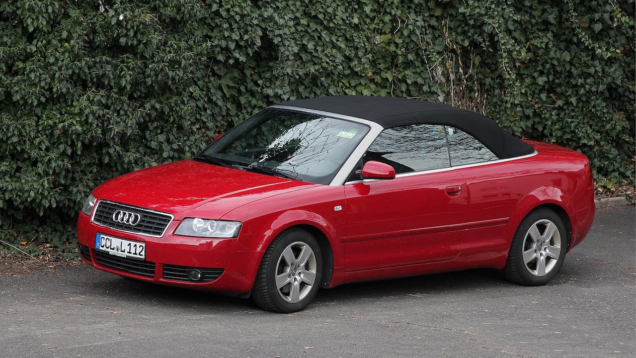 Red Audi A4 Cabriolet with black soft top and German license plate parked on asphalt beside ivy-covered wall