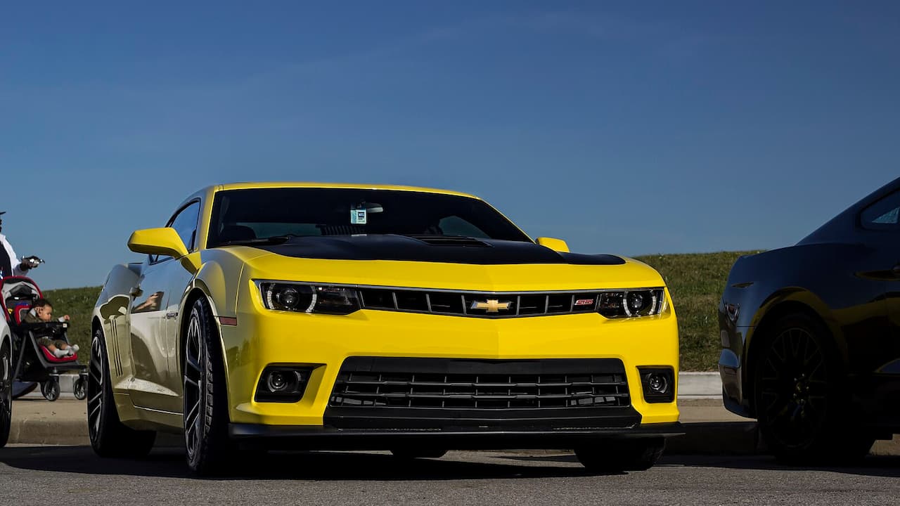 Bright yellow Chevrolet Camaro SS 1LE with black racing stripes parked on asphalt against blue sky