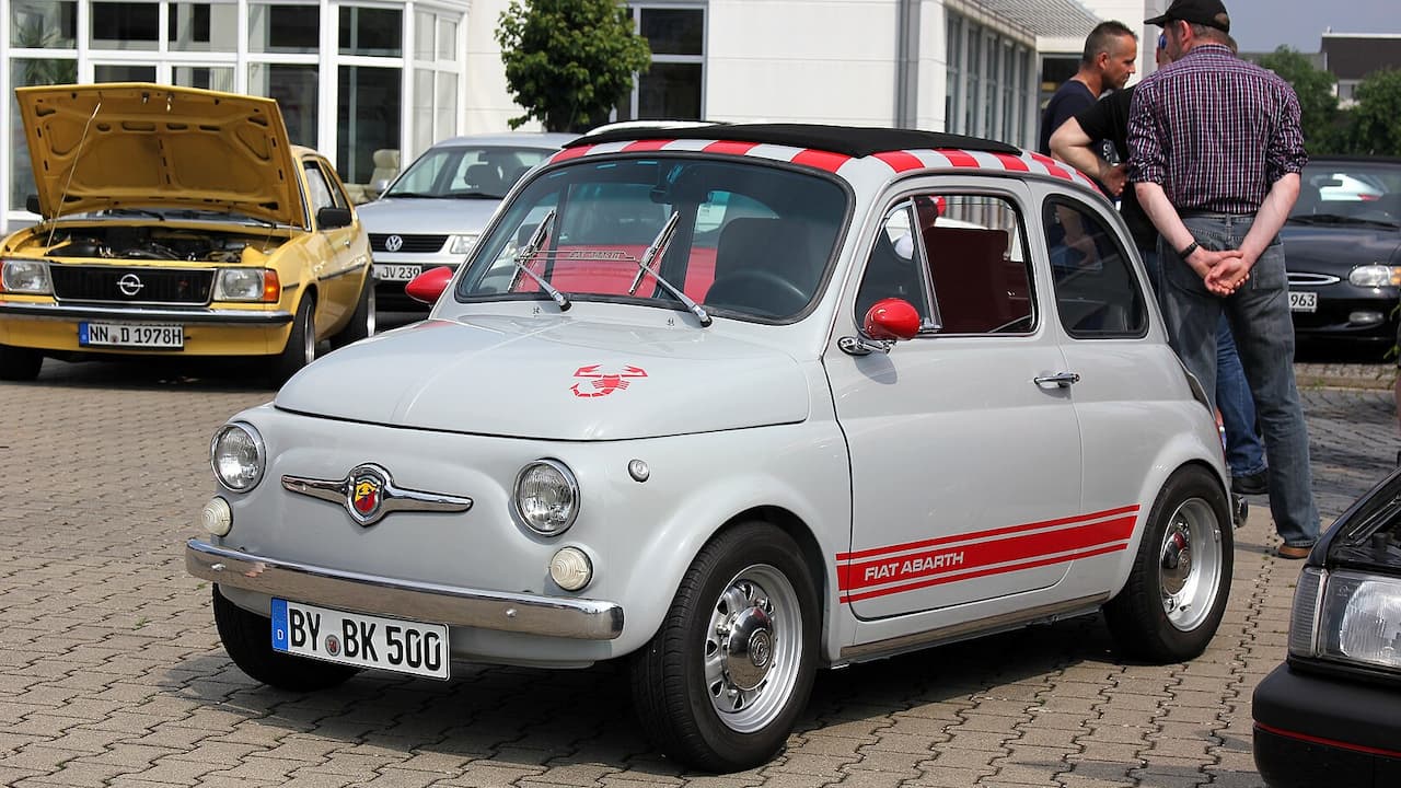 White Fiat 500 Abarth with red racing stripes and checkered roof pattern parked at classic car gathering