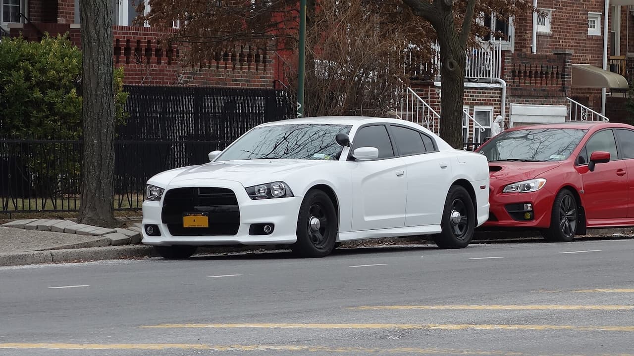 White Dodge Charger unmarked police car with black steel wheels and yellow license plate parked on street