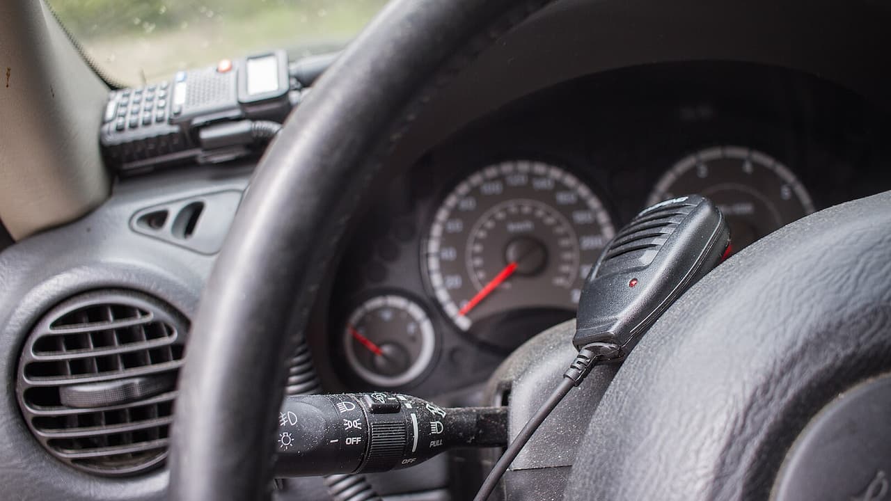 Car interior showing CB radio handset mounted on dashboard with steering wheel, gauges, and headlight control stalk visible