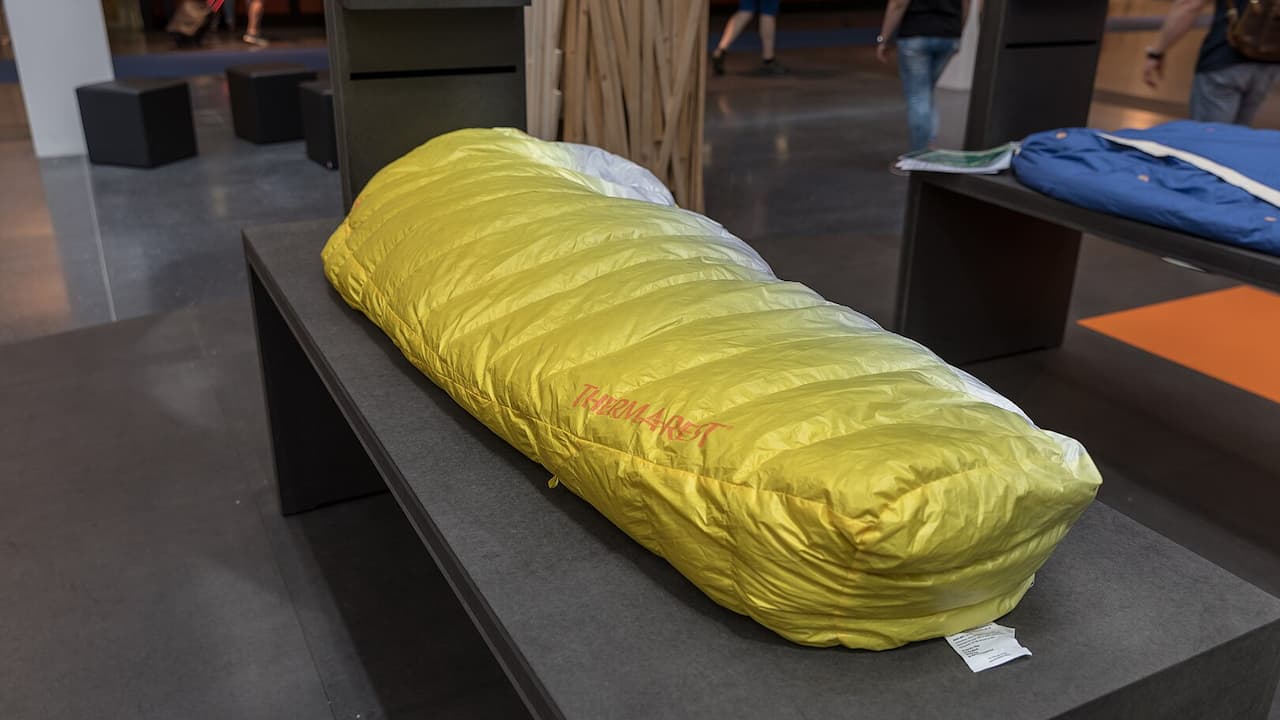 Yellow Therm-a-Rest sleeping bag displayed on black table in outdoor gear store with other equipment visible in background